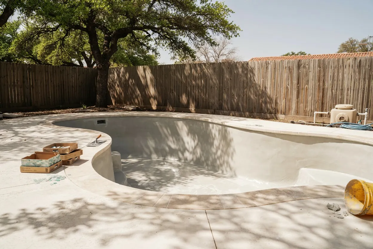 Drained Texas pool mid-renovation with fresh plaster and new tile stacked on the deck