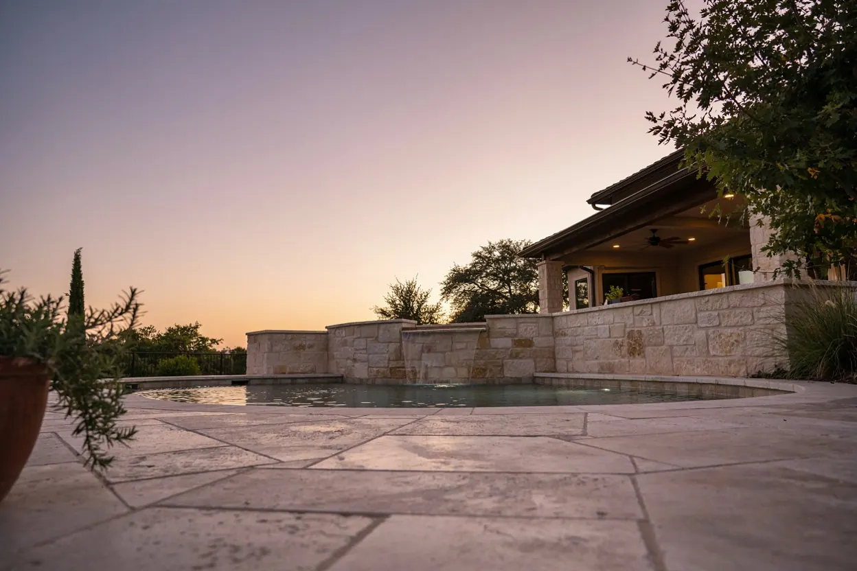 Raised spa spilling into a pool at dusk with a limestone wall